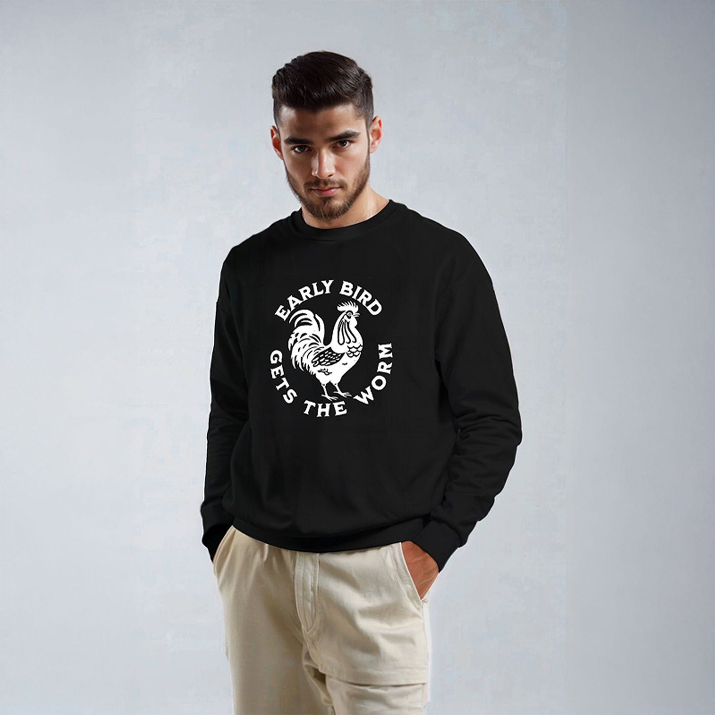 Man wearing black sweatshirt with white rooster graphic and text “Early Bird Gets The Worm,” paired with light beige pants