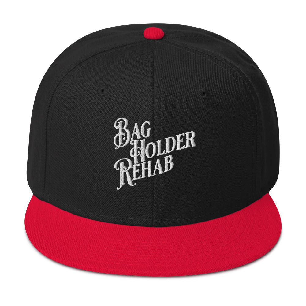 Man wearing black and red baseball cap with embroidered text “Bag Holder Rehab,” tilting brim downward while dressed in a white shirt