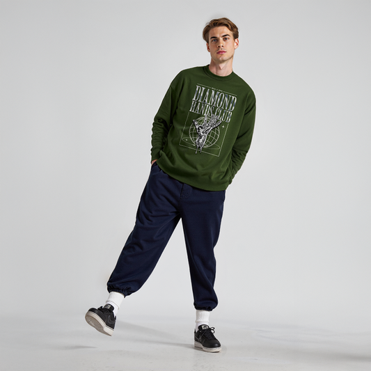 Man wearing green sweatshirt with “Diamond Hands Club” graphic featuring line art and globe grid, paired with navy joggers and black sneakers
