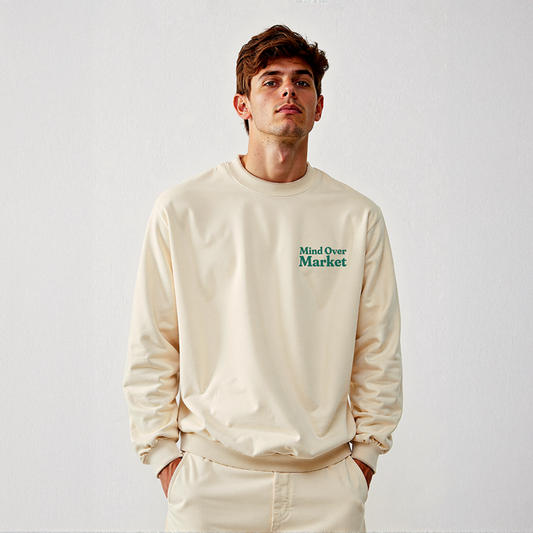 Man wearing cream “Mind Over Market” sweatshirt with hands in pockets, standing against a white background