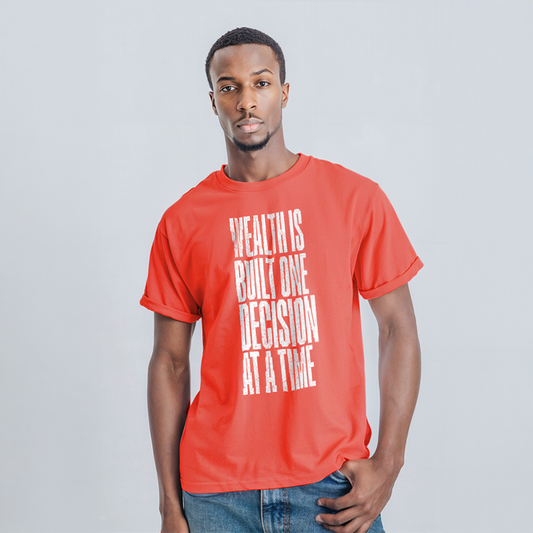 Man wearing red graphic t-shirt with bold vertical white text that reads “Wealth Is Built One Decision At A Time,” paired with jeans
