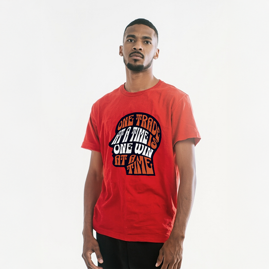 Man wearing red graphic t-shirt with bold text in head-shaped design: “One Trade at a Time, One Win at a Time”
