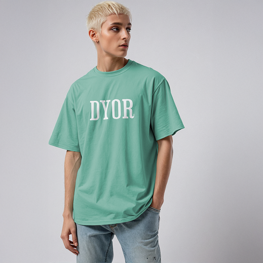 Man wearing mint green “DYOR” t-shirt in bold white letters, paired with light-wash denim jeans in a minimalist studio setting