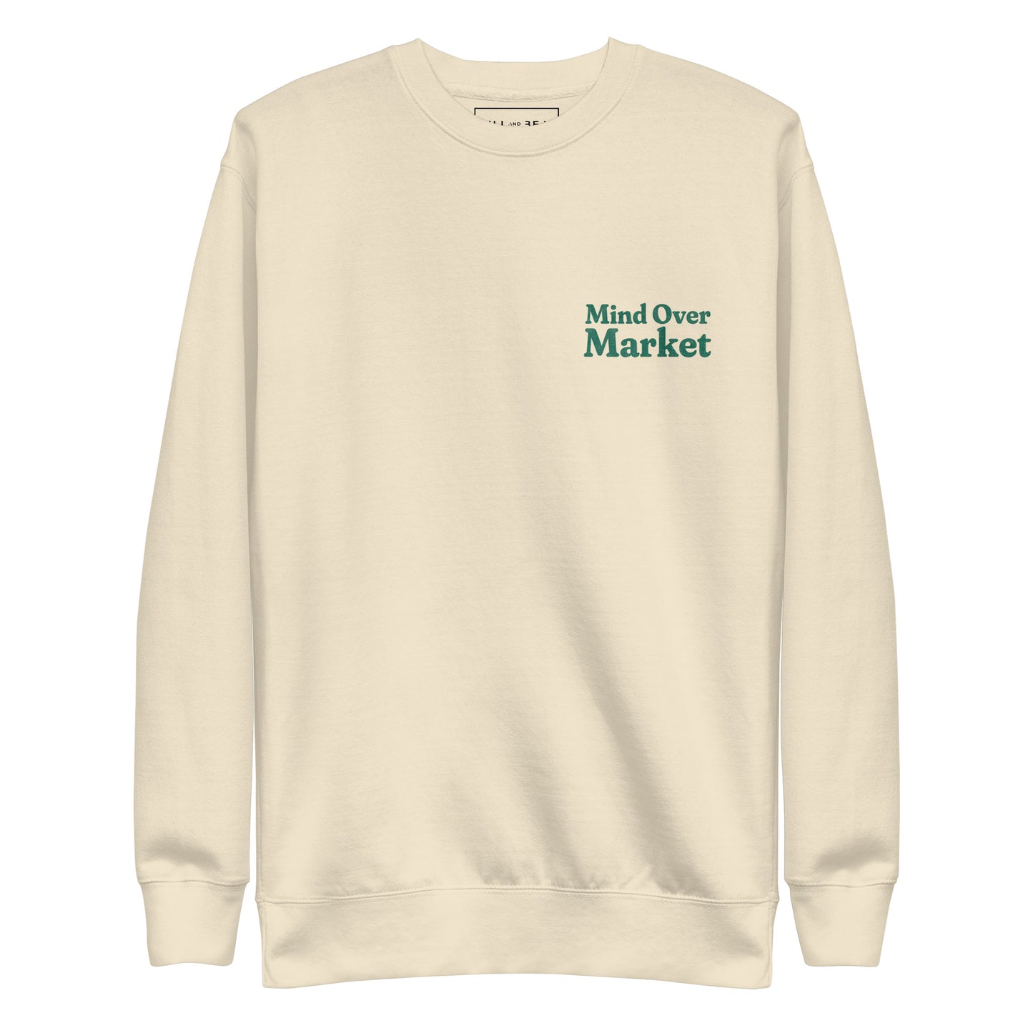 Man wearing cream “Mind Over Market” sweatshirt with hands in pockets, standing against a white background