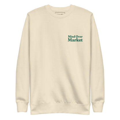 Man wearing cream “Mind Over Market” sweatshirt with hands in pockets, standing against a white background